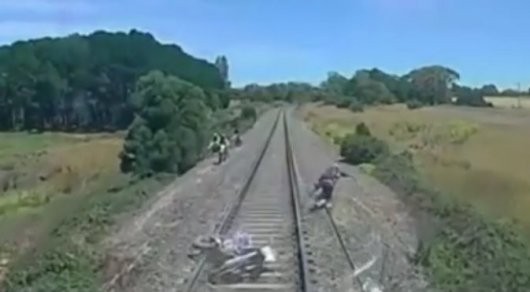 Австралияда мотоциклчини тез юрар поезд босиб кетишига бир баҳя қолди (Видео)