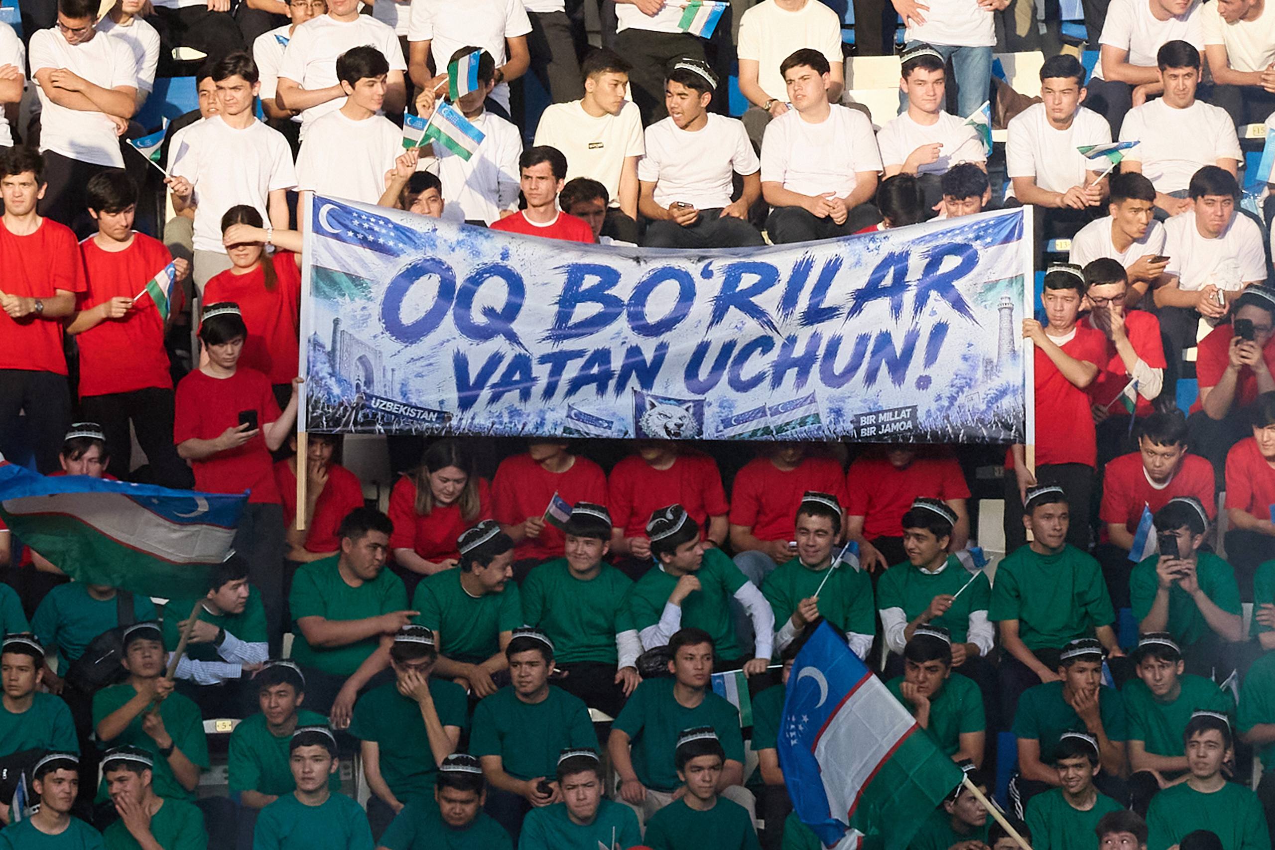O‘zbekistonlik futbol fanatlari stadionda katta banner va bayroqlar bilan jamoani qo‘llamoqda.
