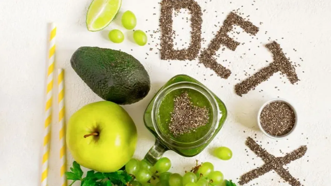 Yashil smuzi, olma, avokado va urug'lardan yozilgan "Detox" so'zi oq fonda turibdi.