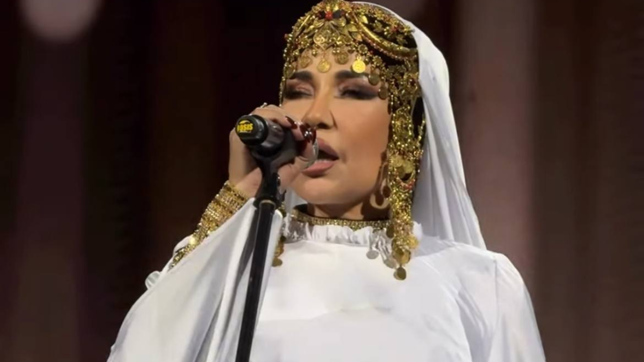 Oq libos va tillarang taqinchoqlardagi ayol mikrofonda qo‘shiq kuylamoqda.