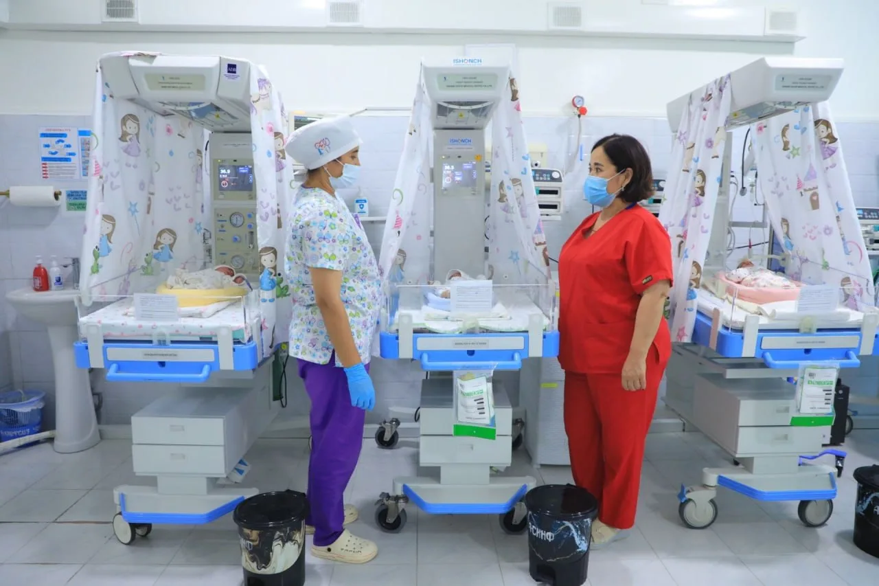 Ikki tibbiyot xodimi neonatologiya bo'limida chaqaloqlar kyuvetlari yonida turibdi.