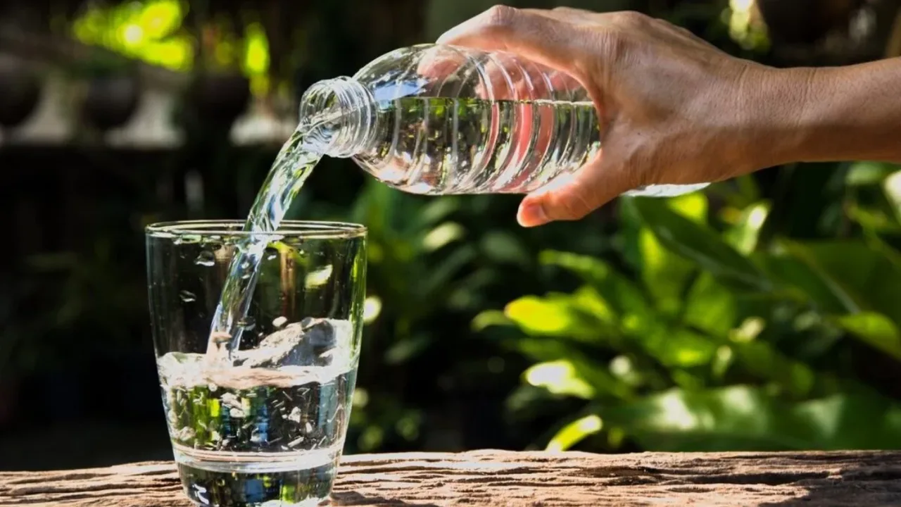Kimdir plastik idishdan shisha stakanga suv quymoqda.
