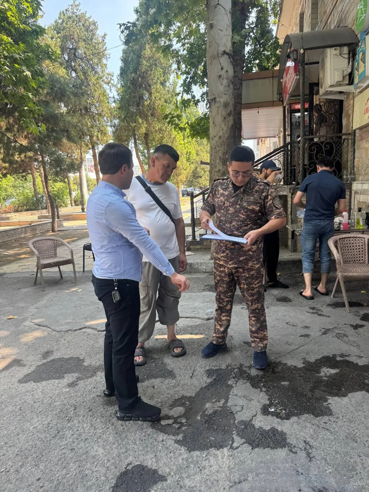 Harbiy kiyimdagi shaxs ko‘chada ikki kishi bilan hujjatlarni ko‘zdan kechirmoqda.