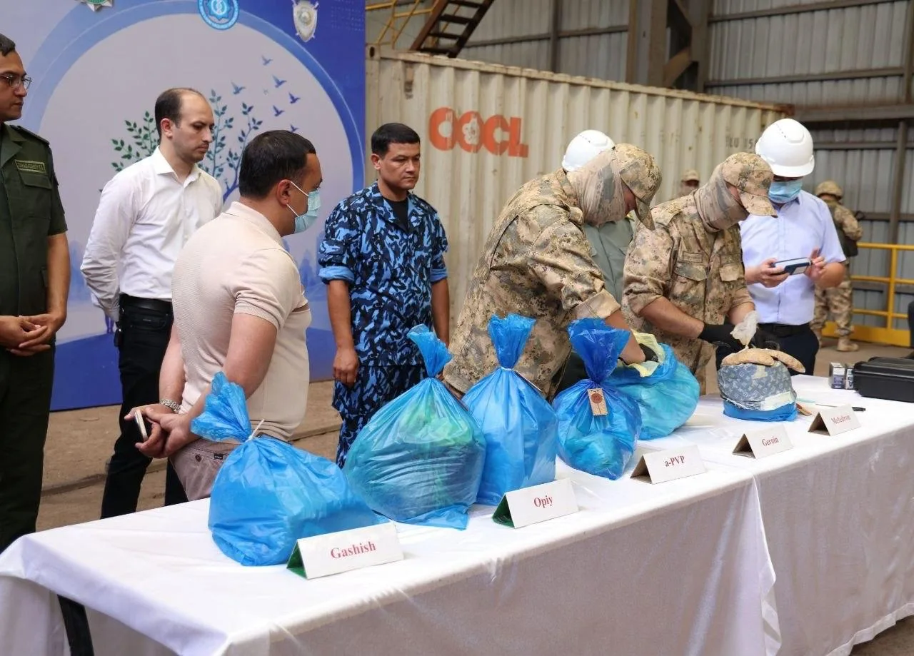 Harbiy kiyimdagi shaxslar ko‘k qoplardagi giyohvand moddalarni ko‘zdan kechirmoqda.
