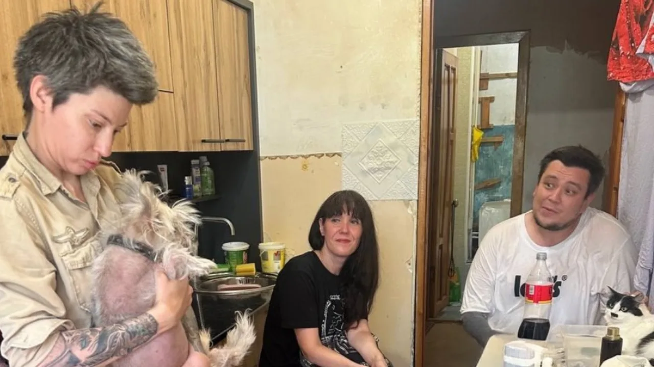 Three people are sitting in the kitchen with a dog and a cat.