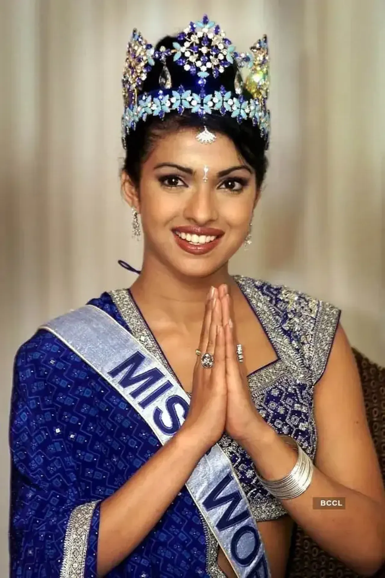 Priyanka Chopra greeting in an Indian style with a crown and sash.