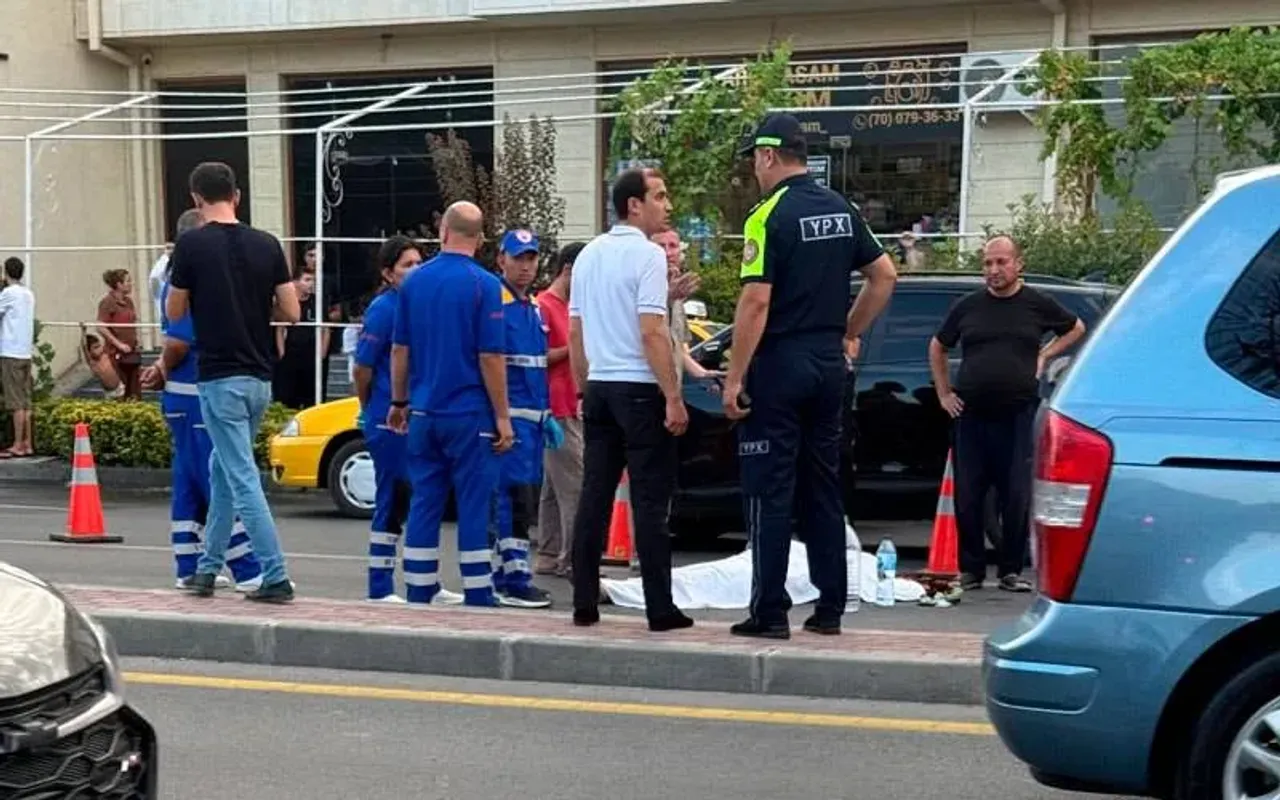 A traffic police officer and ambulance staff stand near a body covered with a white cloth on the side of the road.