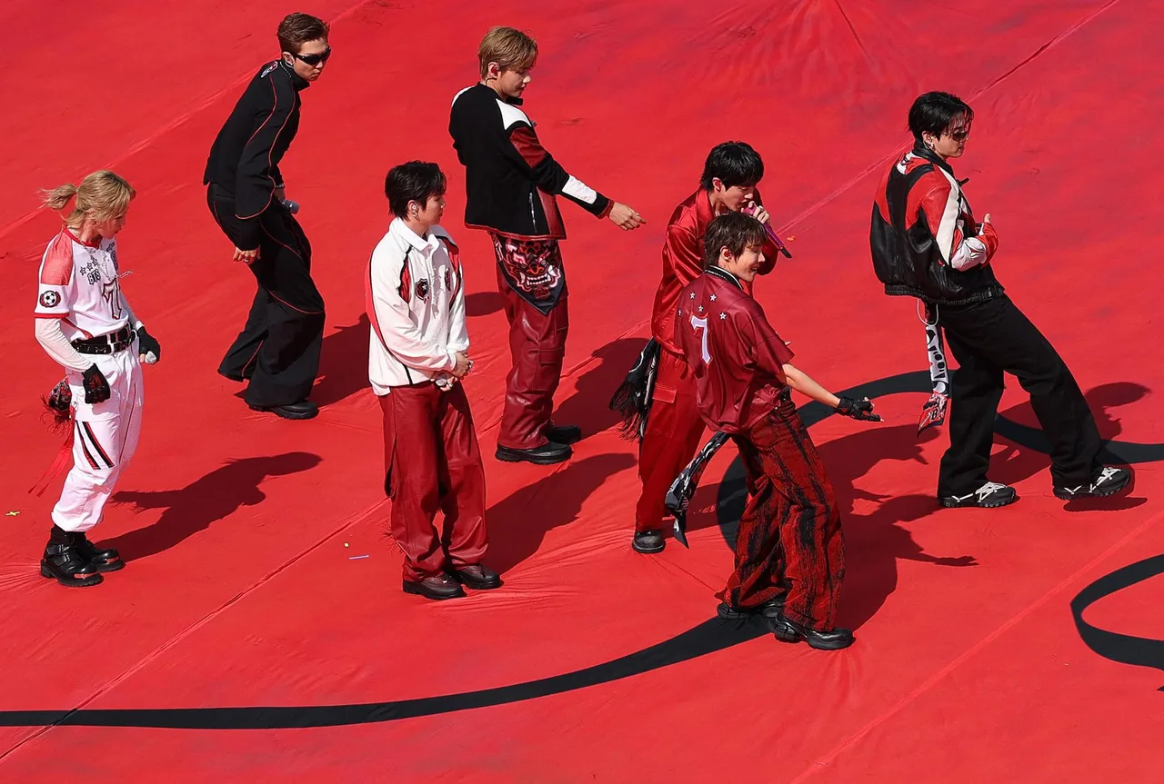 Seven young men in various colored and styled clothes standing against a red background.