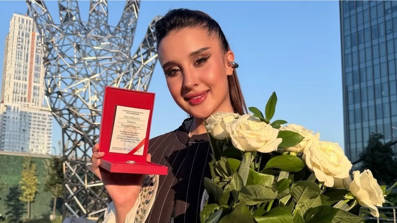 Madina Fayzullayeva oq atirgullar va "O'zbekiston belgisi" nishoni bilan tushgan surat.