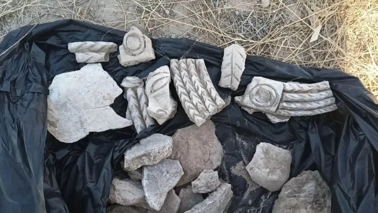 Qora polietilen ustida naqshli qadimiy tosh va ganch parchalari yotibdi.