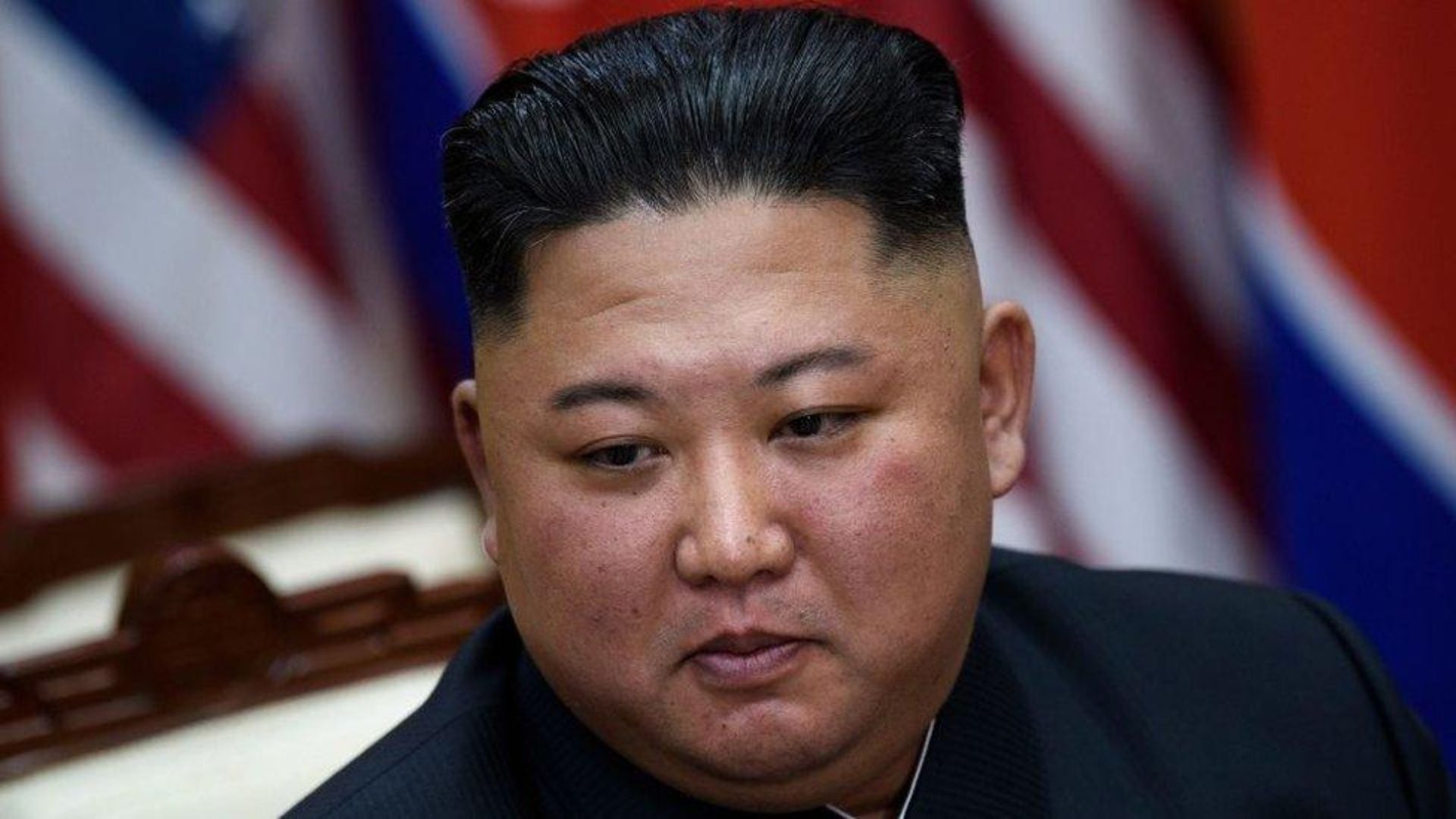 Shimoliy Koreya yetakchisi Kim Chen In bayroqlar fonida yaqindan tasvirlangan.
