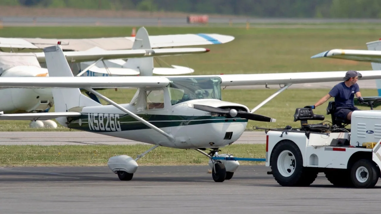 Oq-yashil rangli Cessna samolyoti aeroportda kichik traktor yordamida tortilmoqda.