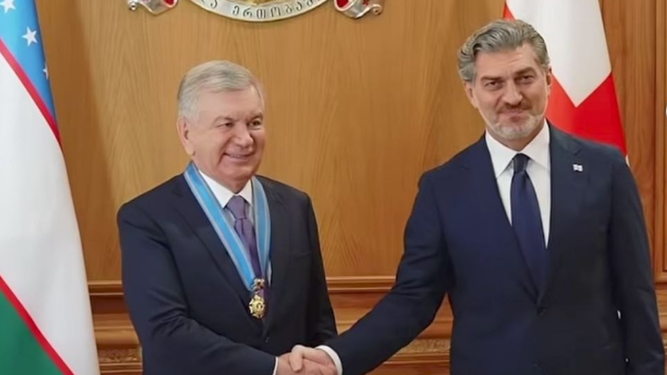Shavkat Mirziyoyev va Gruziya vakili bayroqlar oldida qo‘l berib ko‘rishmoqda.