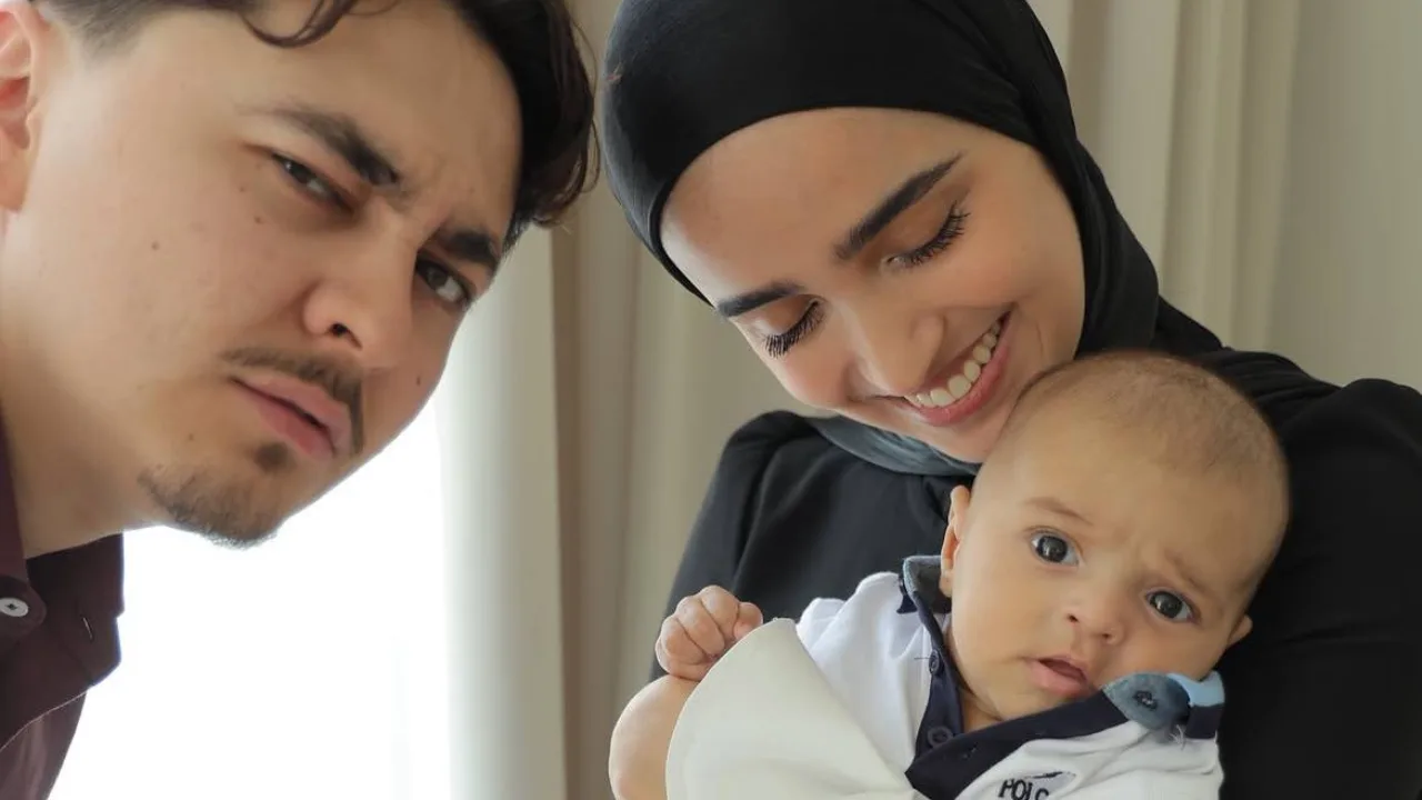 The couple is holding their little baby in their arms and looking at him.