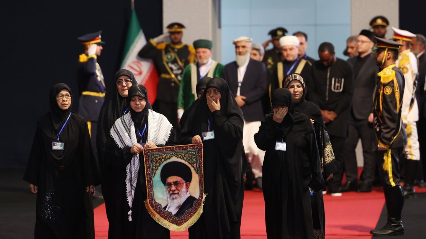 Qora kiyimdagi ayollar Khamenei portretini ko'tarib, tantanali marosimda yurib borishmoqda.