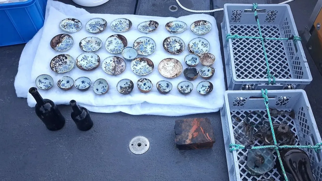 Oq matoda koʻk naqshli piyola va likopchalar, yonida shisha butilkalar turibdi.