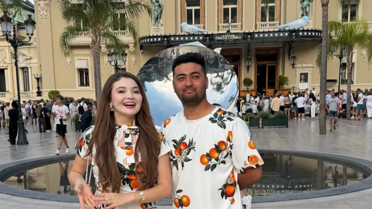Monte-Karlo kazinosi oldida apelsin rasmli köylak kiygan yigit va qiz turibdi.