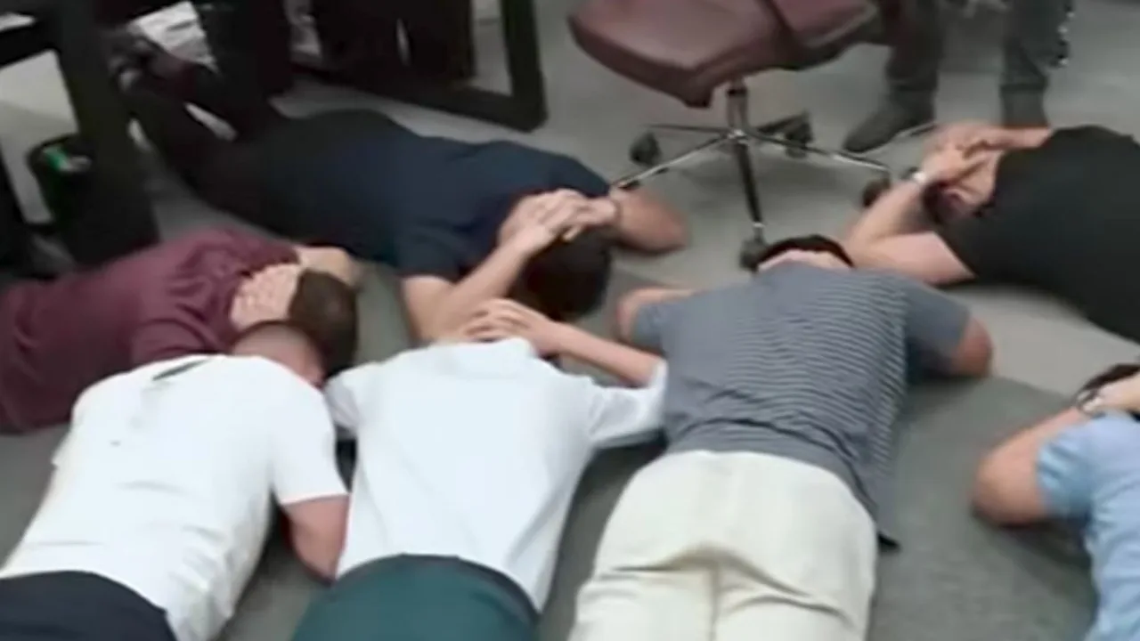 Several people are lying face down on the office floor.