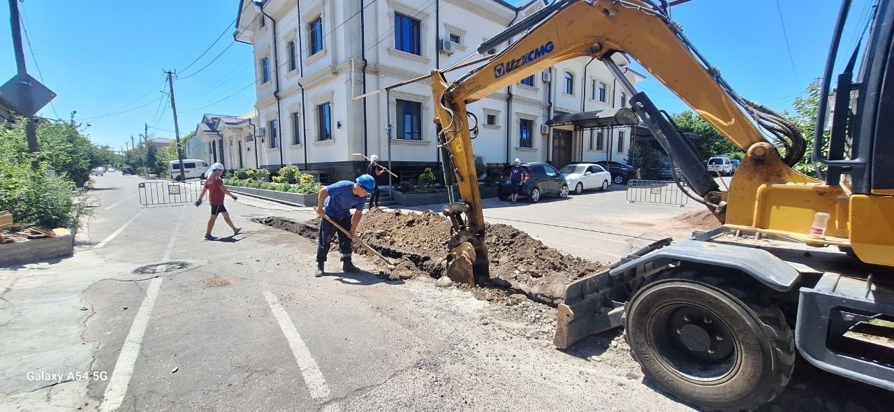 Ishchilar va ekskavator ko‘cha chetida qazish ishlarini olib bormoqda.
