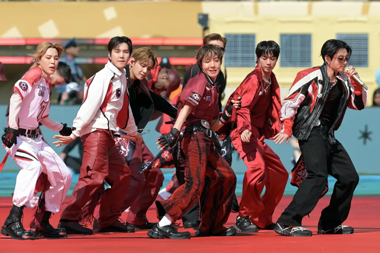BTS group members dancing on stage in red and white outfits.
