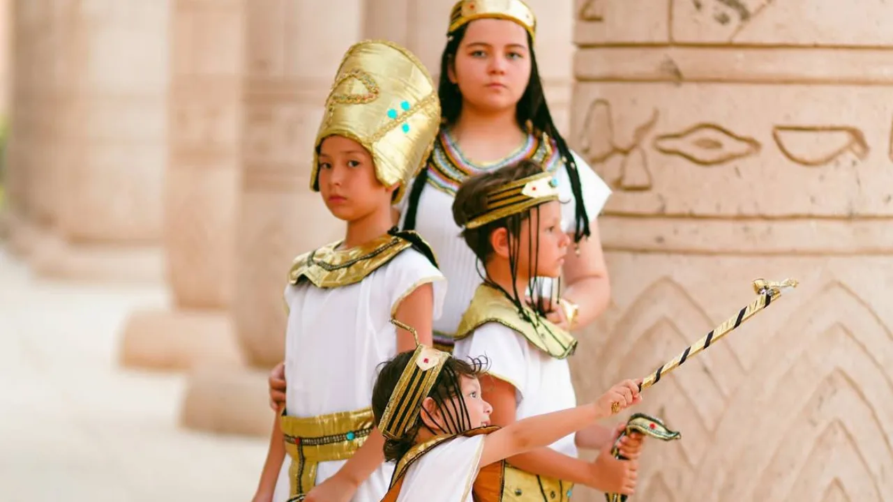 Children wearing Ancient Egyptian clothes standing by columns with hieroglyphs.