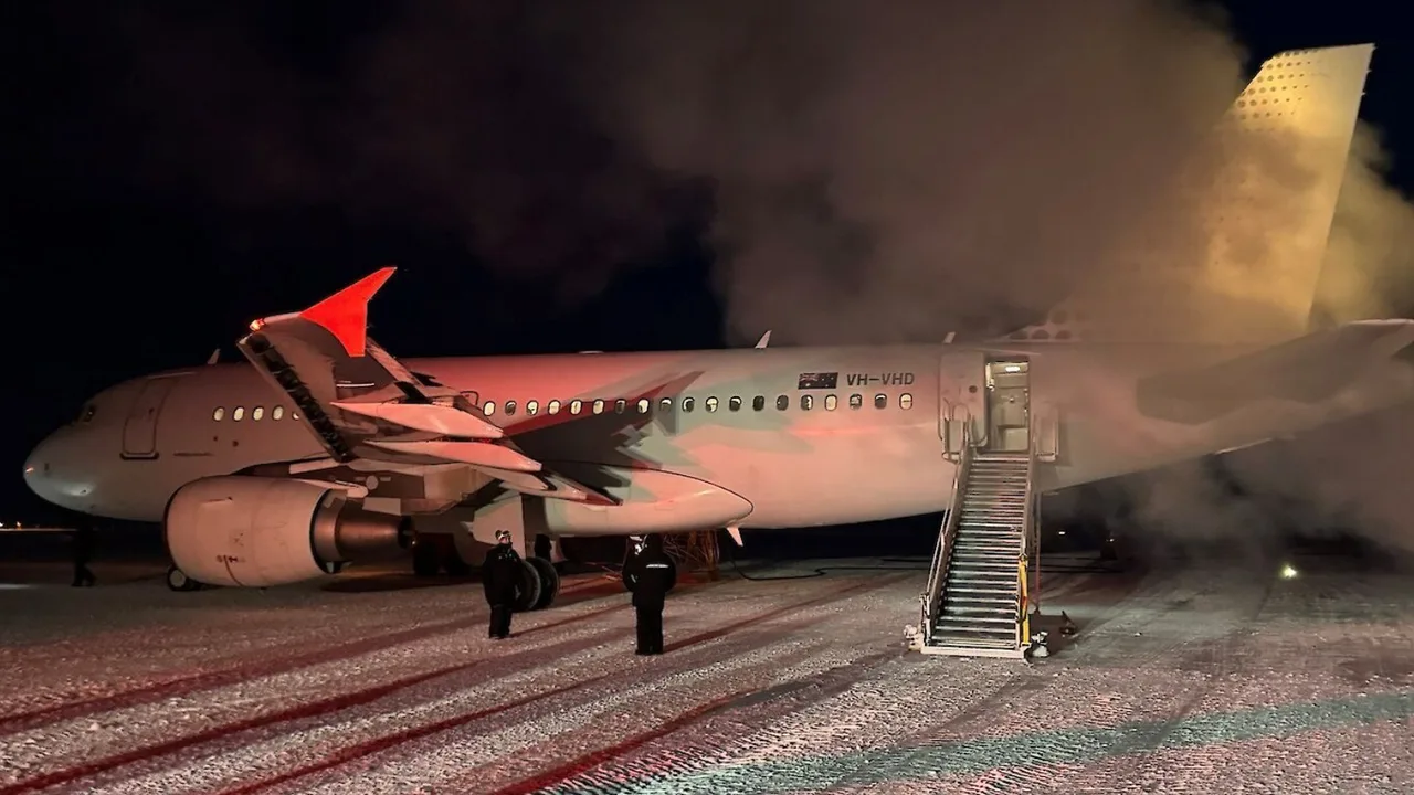 Qorong'uda aerodromda turgan va dumidan tutun chiqayotgan Jetstar samolyoti.