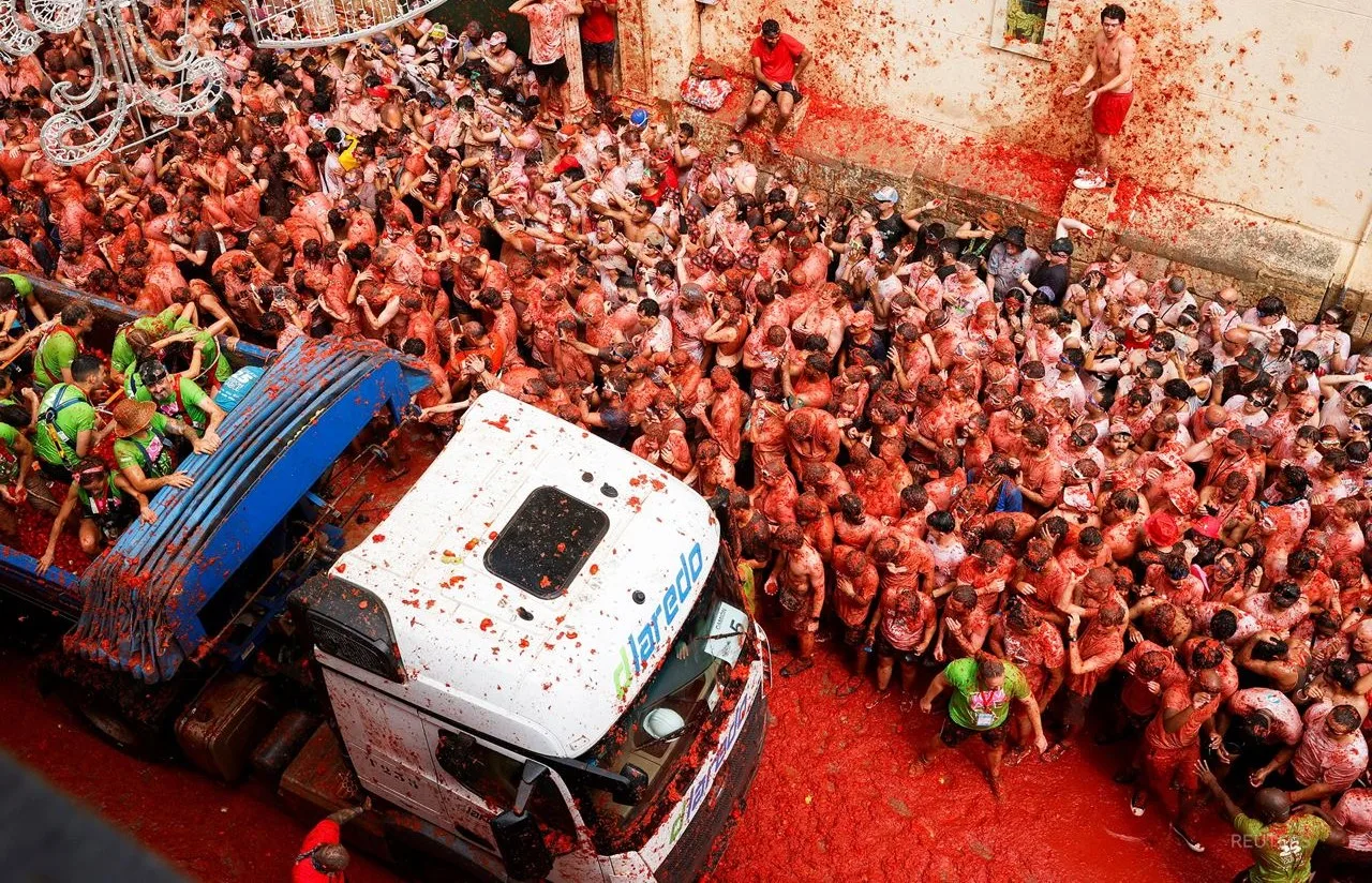 La Tomatina festivalida odamlar yuk mashinasi yonida bir-biriga pomidor otmoqda.