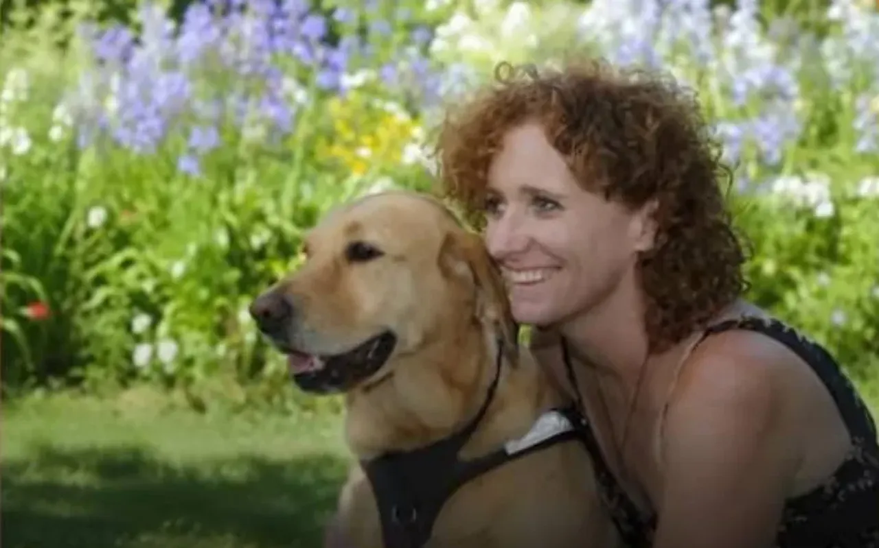 Jingalak sochli ayol bog‘da labrador iti bilan birga tabassum qilib turibdi.