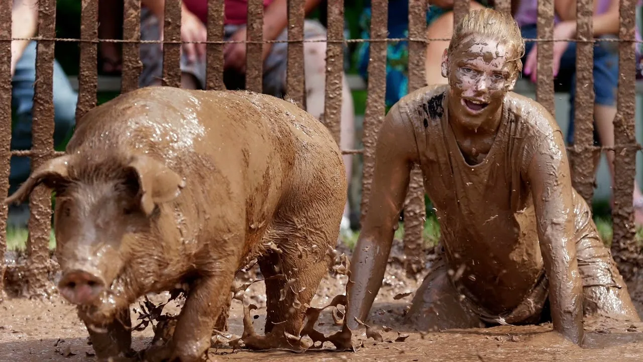 A mud-covered woman chasing a pig through the mud.