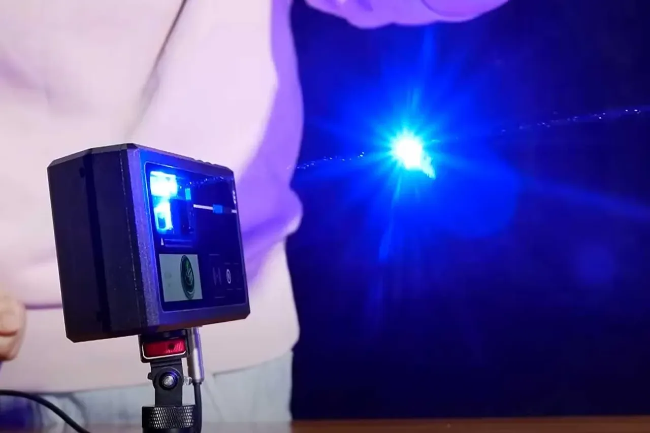 Tripodga o‘rnatilgan ko‘chma lazerli printer ko‘k nur taratmoqda.