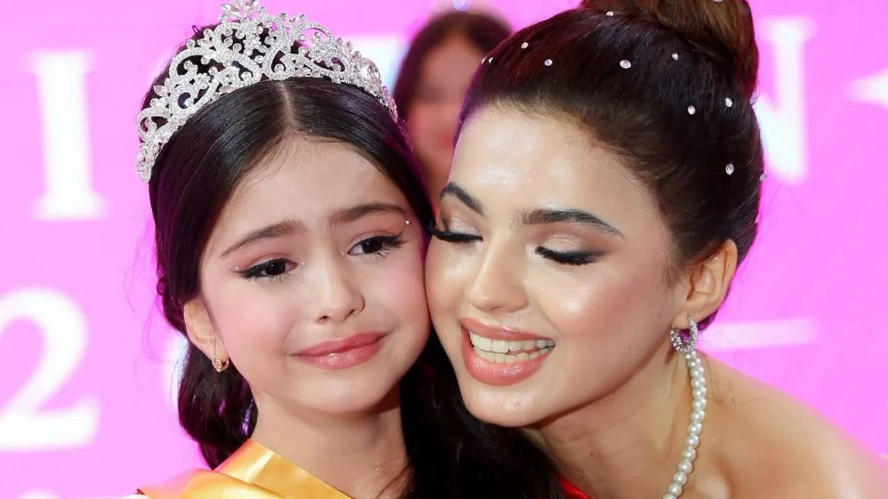 A crowned young girl and a smiling woman standing beside her.
