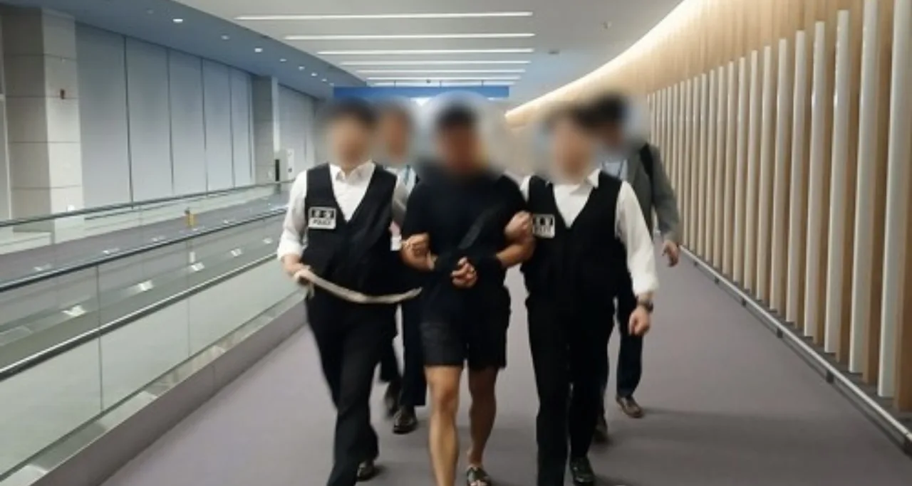 Two police officers escorting a person in black clothing through an interior corridor of a building.