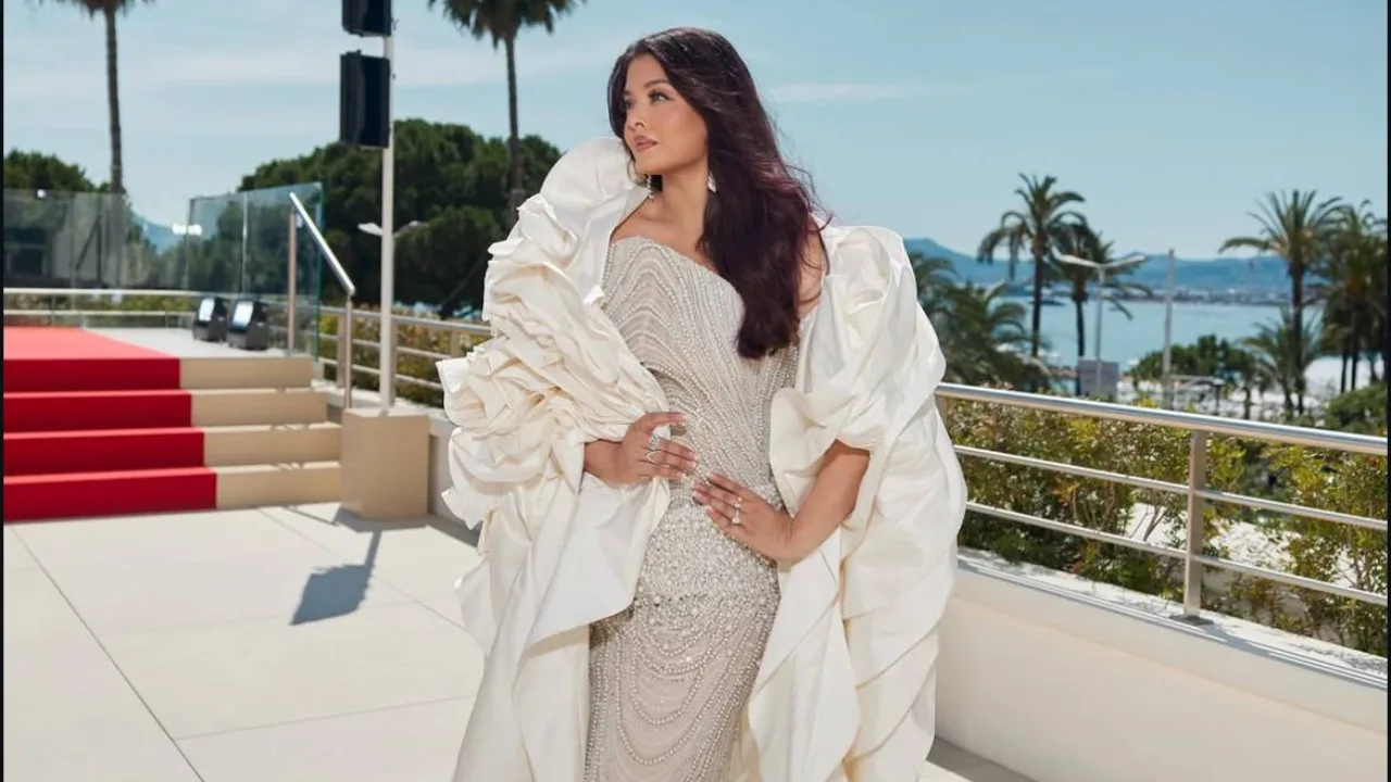 A woman in a white and silver gown standing beside the red carpet.