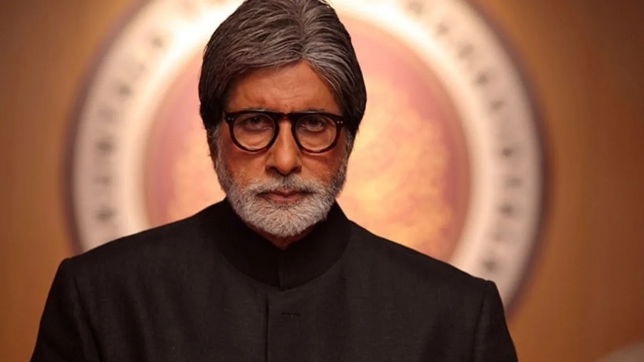 Amitabx Bachchan qora kostyum va ko‘zoynakda jiddiy qiyofada turibdi.