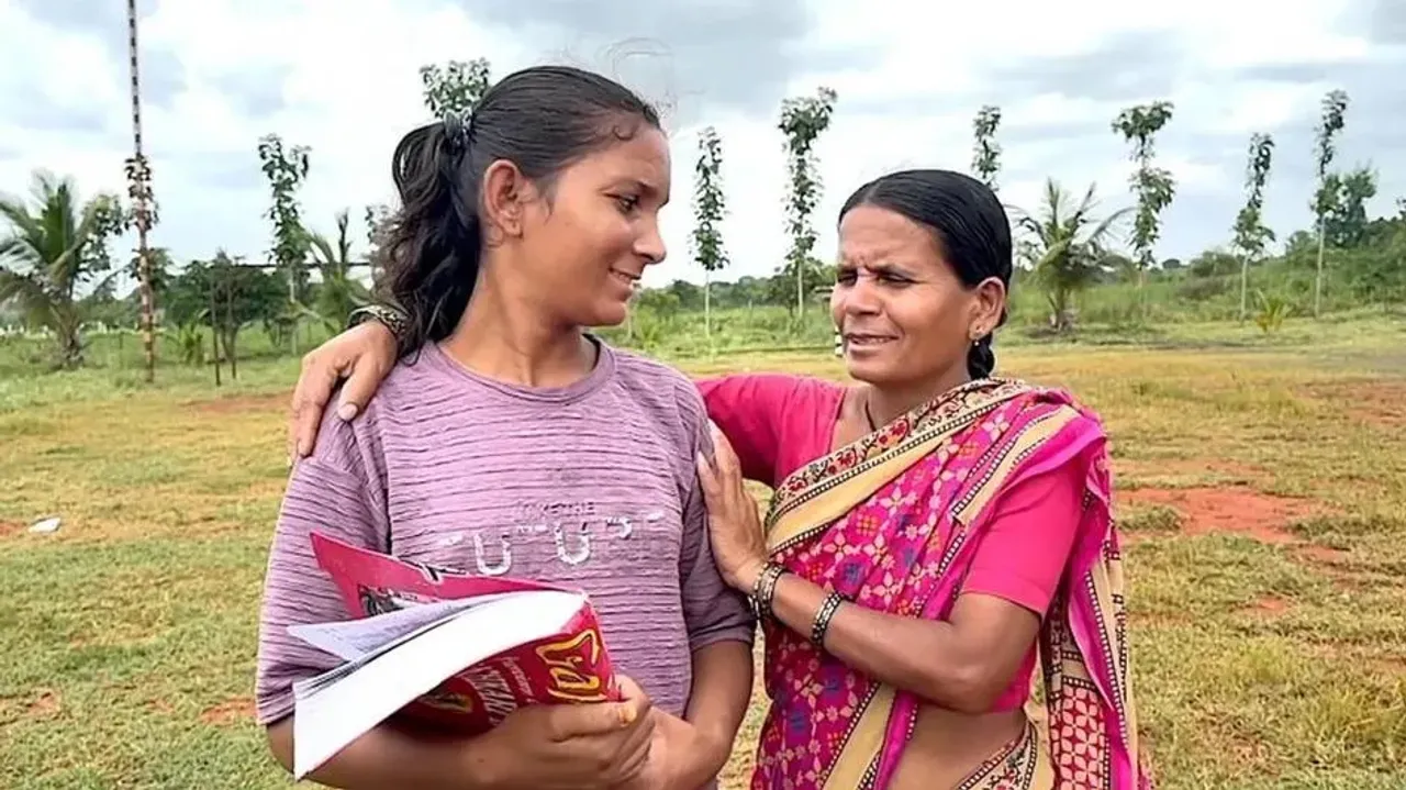 A woman in a sari in a field with a girl holding a book