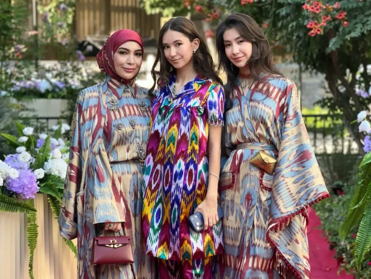 Three women in adras and atlas dresses posing together in a garden.