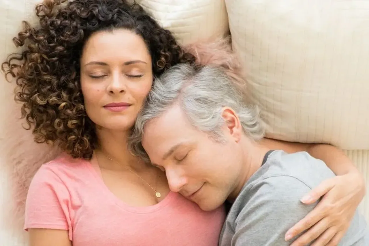 A woman and a man lying down, hugging each other with their eyes closed.