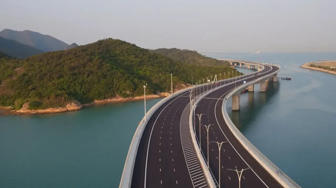 A multi-lane curved bridge passing over the sea and green hills.