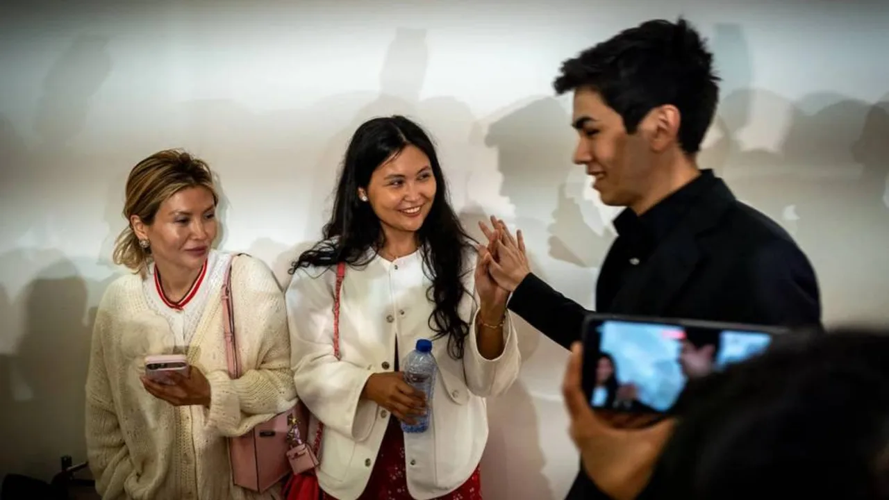 Three young people are talking in front of a white wall.