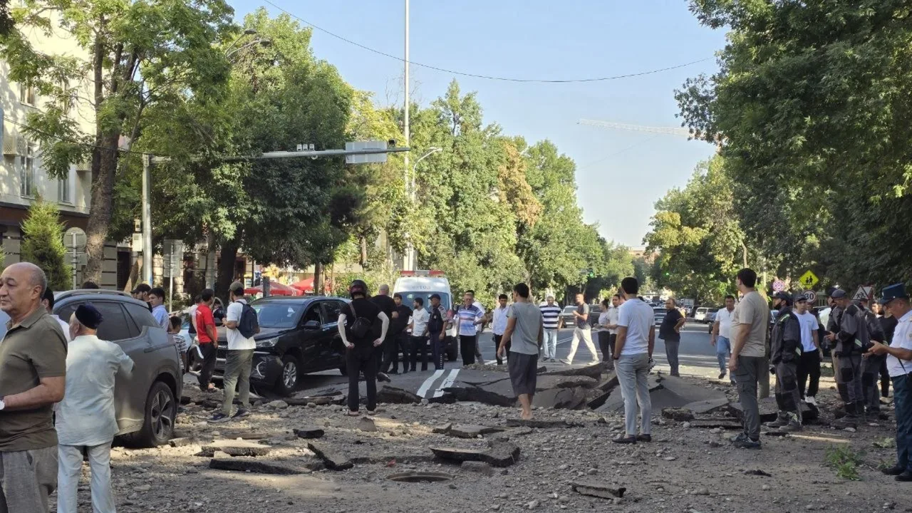 Odamlar ko'chada asfalt qoplamasining o'pirilishi natijasida yuzaga kelgan vayronani kuzatmoqda.