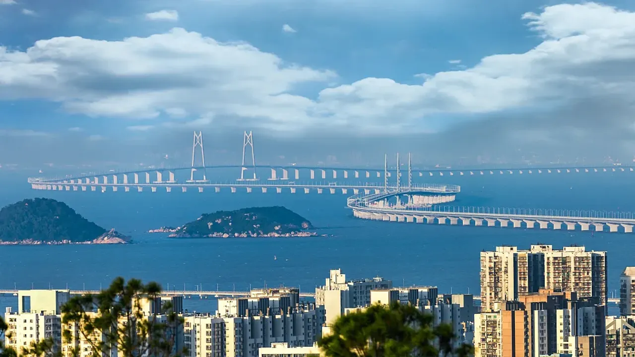 A long bridge passing over the sea, distant islands, and a city landscape.