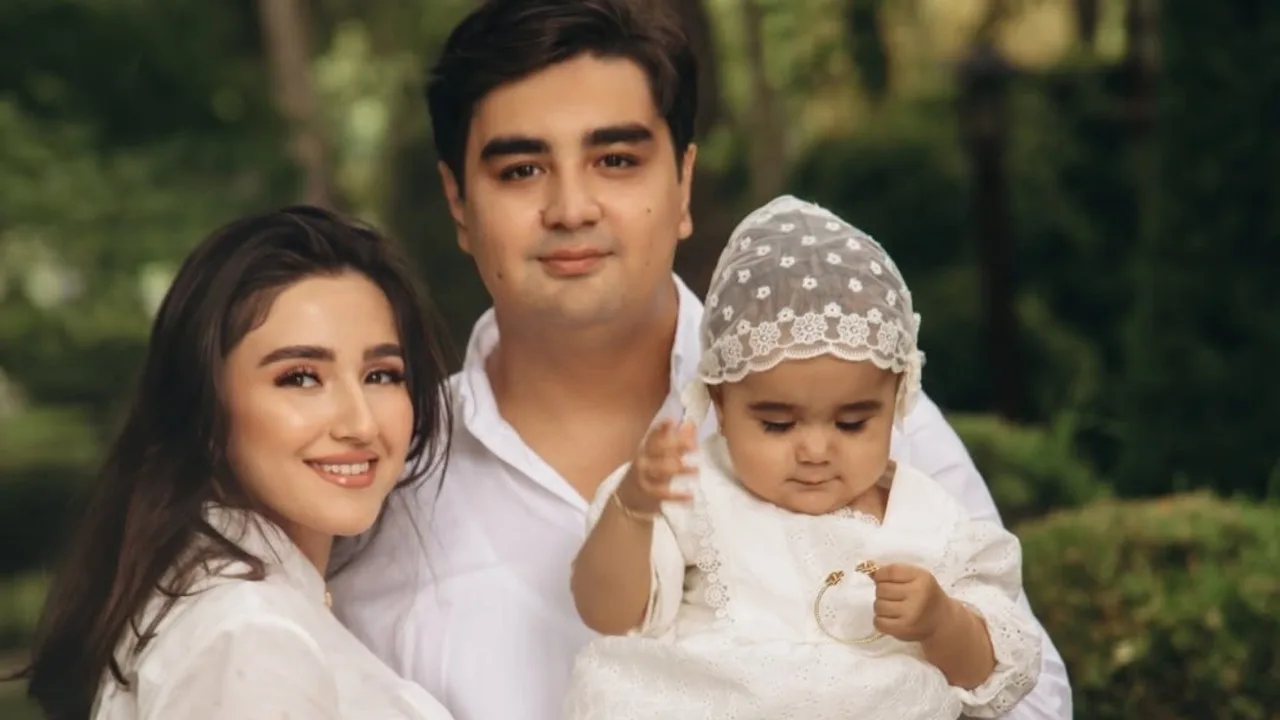 Oq kiyimdagi yosh oila tabiat qo‘ynida chaqaloq bilan tushgan surat.