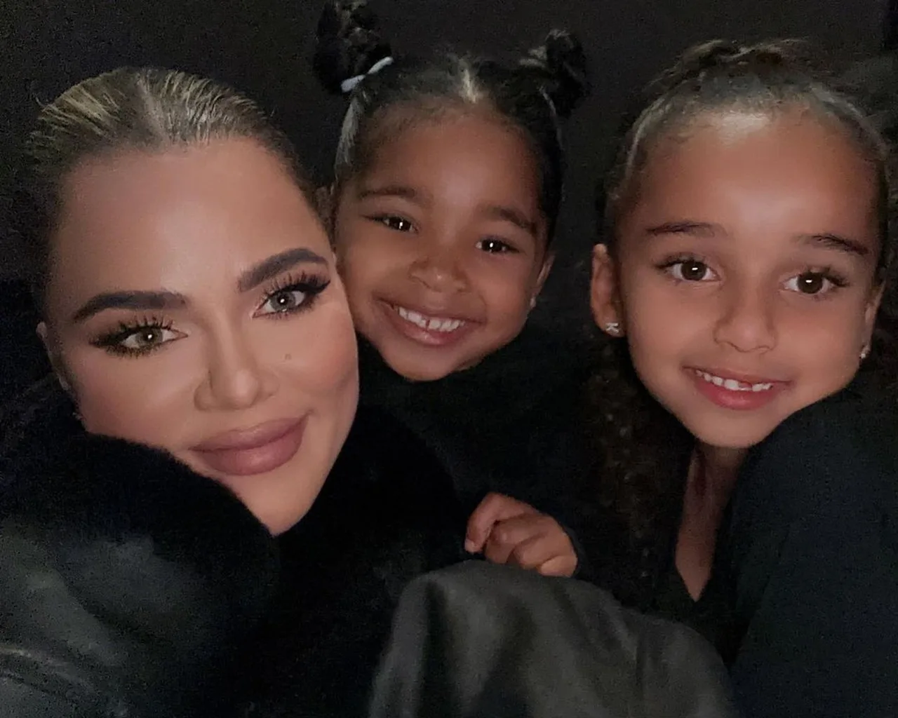 Khloe Kardashian ikki yosh bola bilan qorong'i fonda selfi tushmoqda.