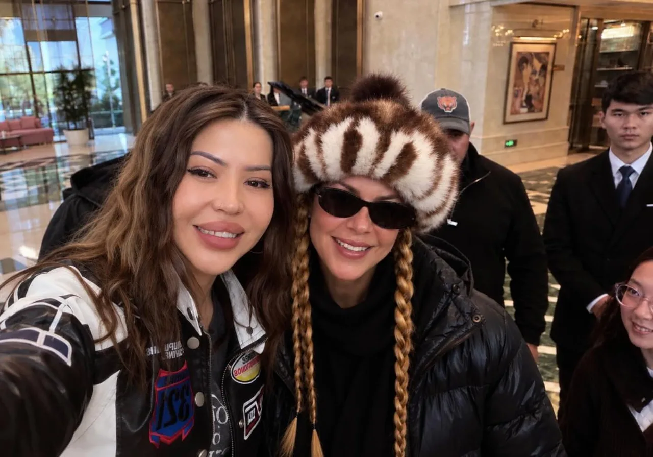 Ikki ayol binoning ichida selfi tushmoqda, ulardan biri mo‘ynali telpakda.