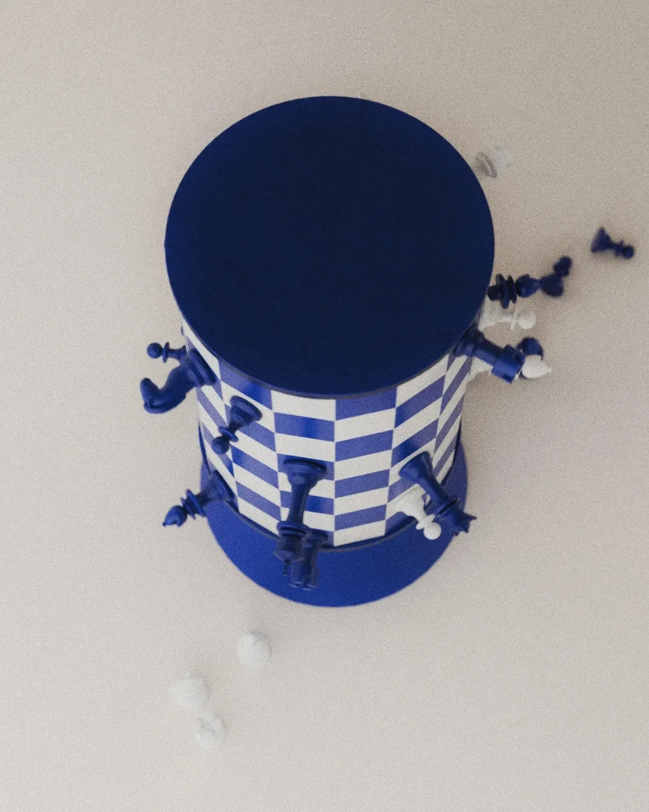 A blue-white checkered cylindrical chessboard with chess pieces attached.