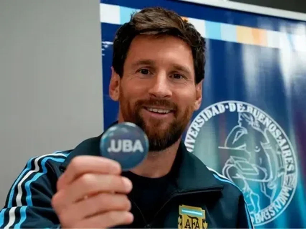 Lionel Messi holding a pin with the UBA logo.
