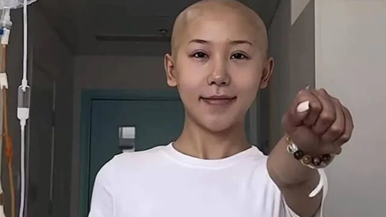 A woman with shaved head in a hospital smiling with her fist extended forward.
