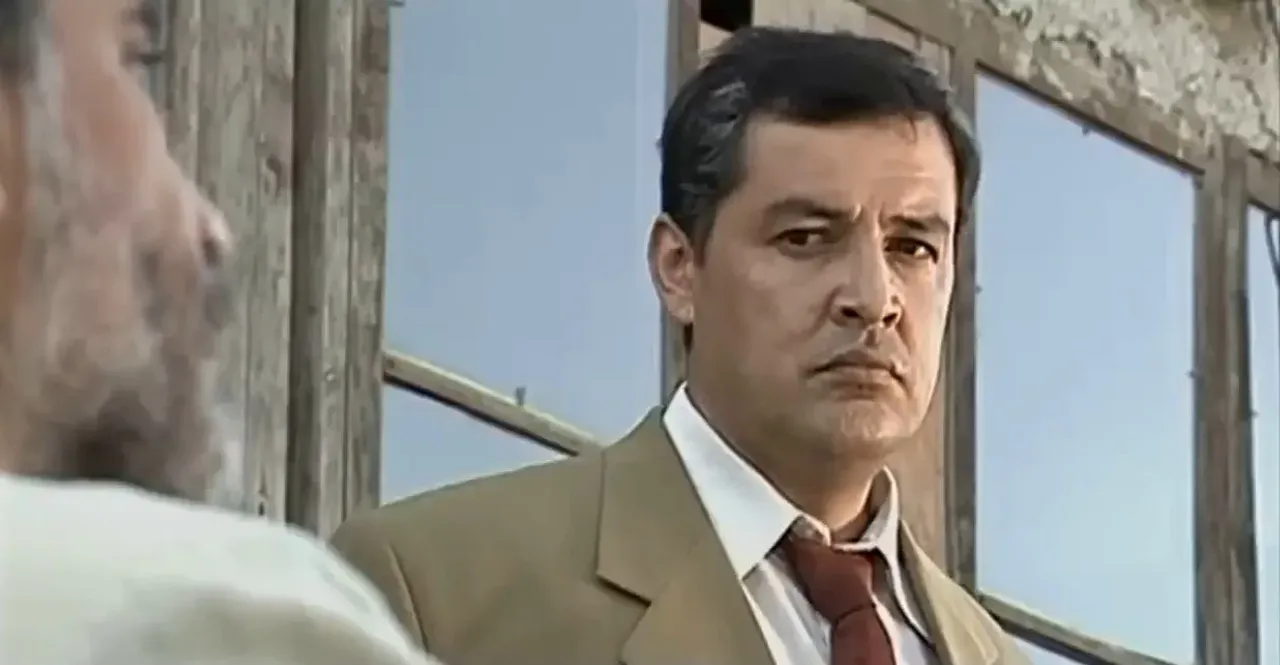 Kostyum va galstuk taqqan kishi jiddiy nigoh bilan qarab turibdi.