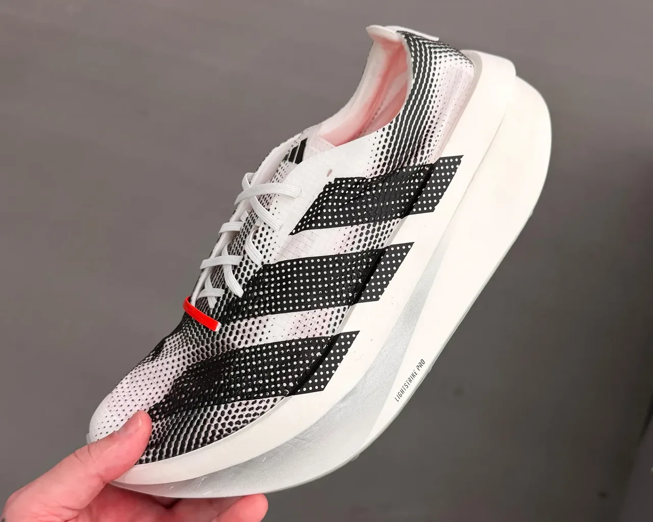 Qora va oq rangli, qalin poshnali Adidas Adizero yugurish poyabzali.