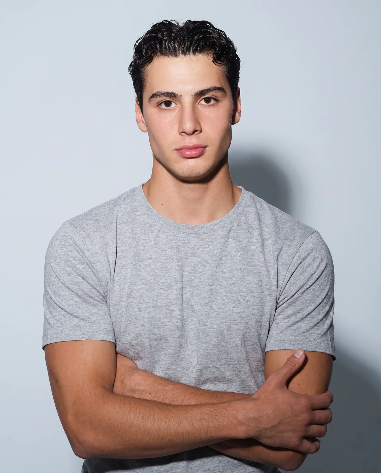 A dark-haired young man in a gray t-shirt with his arms crossed.